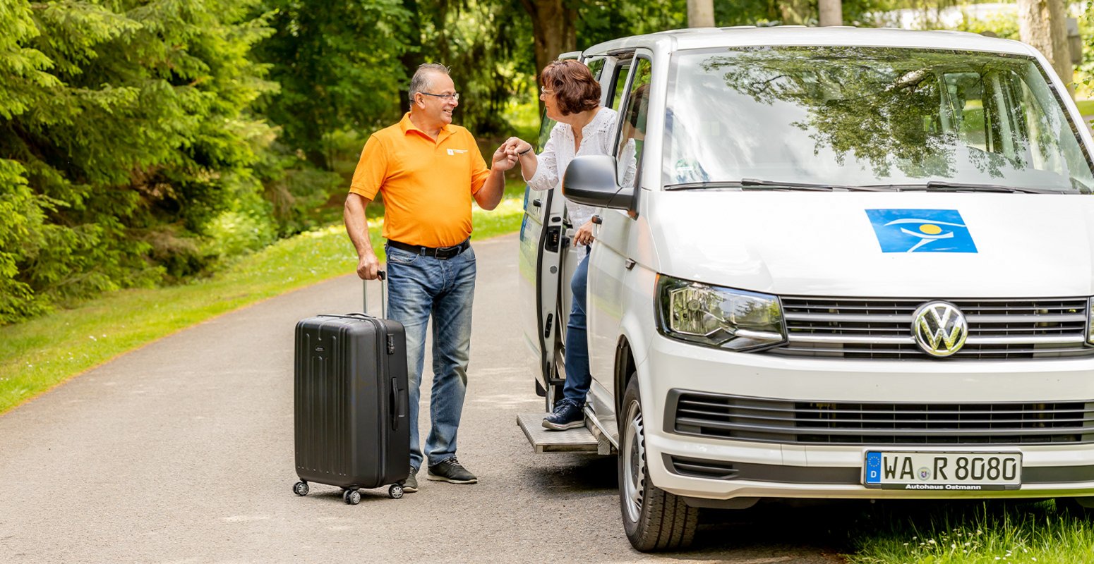 Fahrer mit Koffer in der Hand hilft Dame aus dem HQ Transfer heraus