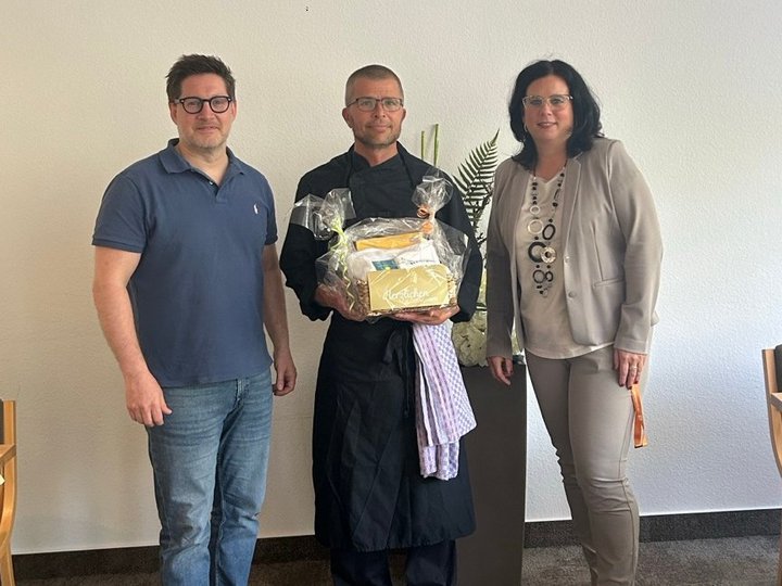 Christian Beulich steht neben Verwaltungsleiterin Anja Hölscher und Geschäftsführer Thomas Albrecht, die ihm einen Präsentkorb überreichen. Er feiert sein 10-jähriges Jubiläum in der Helenenquelle.