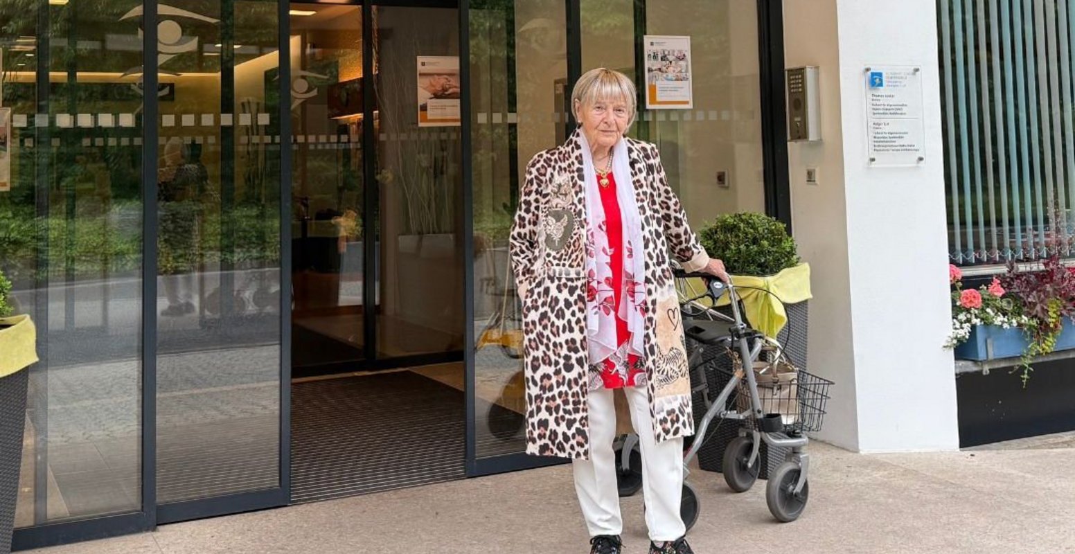 Renate Vehovsky in der Helenenquelle Renate Vehovsky lächelt in die Kamera während sie vor dem Eingang der Helenenquelle steht.