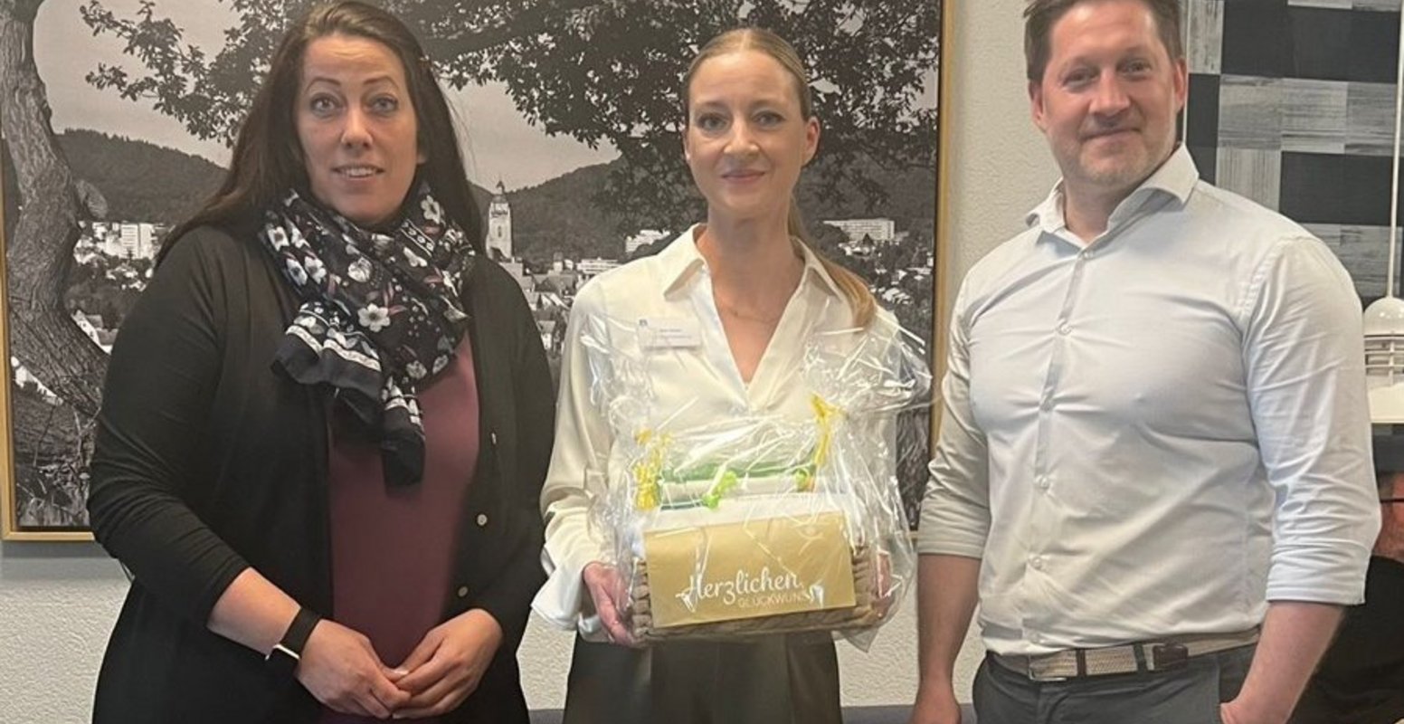 10-jähriges Jubiläum von Nina Rasch Nina Rasch steht neben Geschäftsführer Thomas Albrecht und Verwaltungsleiterin Martina Kluth, die ihr einen Präsentkorb überreichen. Sie feiert ihr 10-jähriges Jubiläum als Teil des Rezeptionsteams in der Klinik Reinhardsquelle.